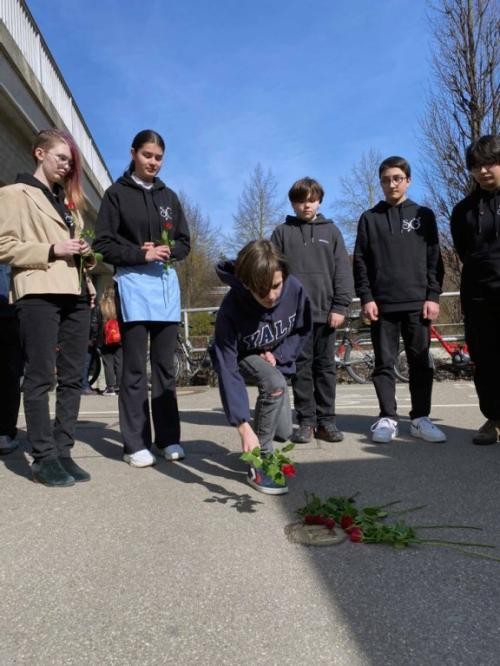 Schülerinnen und Schüler legen Rosen nieder.