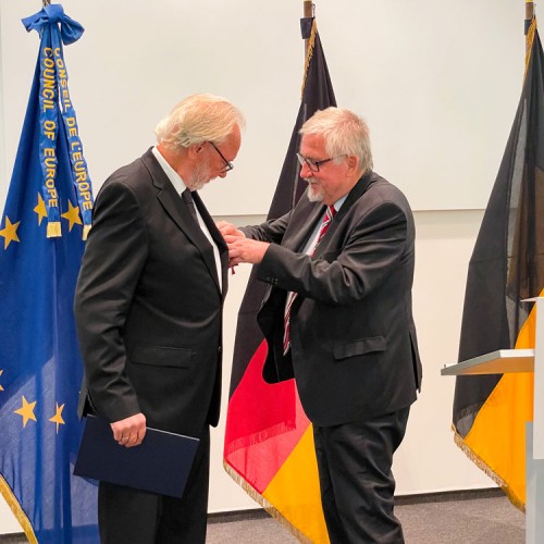 Staatssekretär des Innenministeriums Julian Würtenberger steckt Manfred Neumann das Bundesverdienstkreuz am Bande an. Foto: Stadt Heidenheim